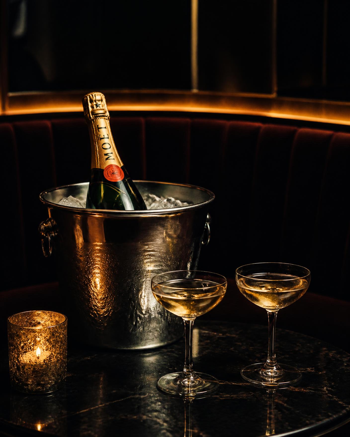 Champagne bottle on ice with two coupe glasses in a velvet VIP booth